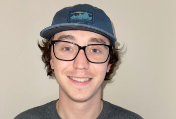 close-up portrait of a young man in a blue cap and dark-rimmed glasses