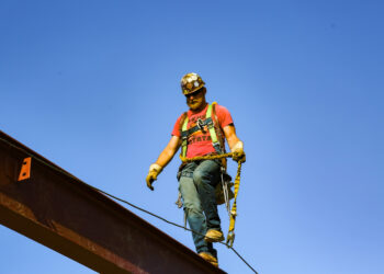 male construction worker walks across steel girder with blue sky in background
