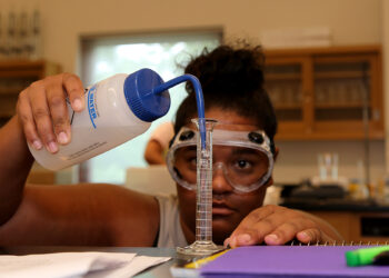 female student wearing goggles siphons liquid into test tube in lab
