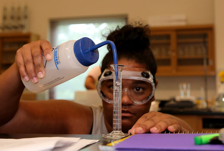female student wearing goggles siphons liquid into test tube in lab