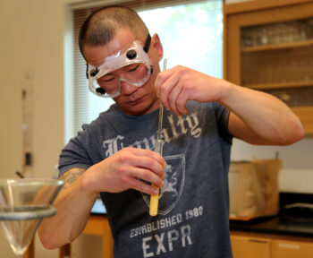 man in chemistry lab wearing goggles with catheter and test tube