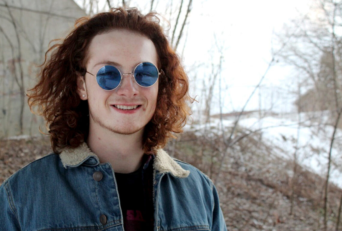 red-haired man wearing sunglasses smiles at camera on a winter day
