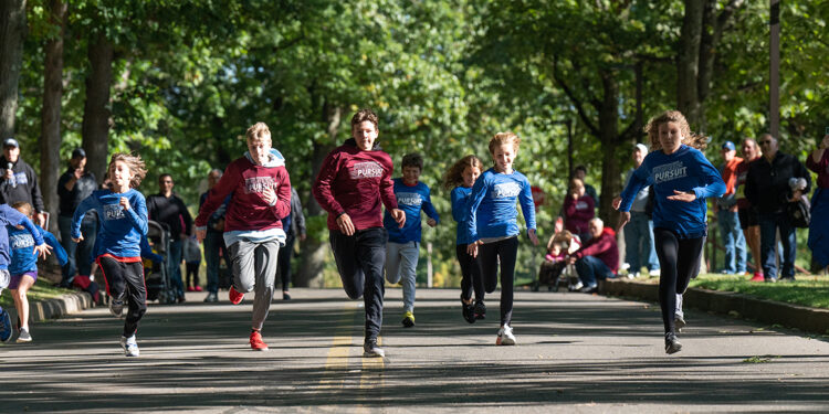 children run in race under a canopy of oak trees down a paved roadway