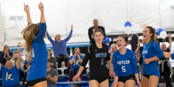 four volleyball players celebrate on court with crowd in background