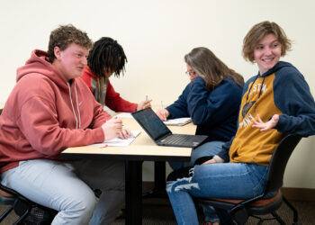 four young people sitting at a table in hoodies.