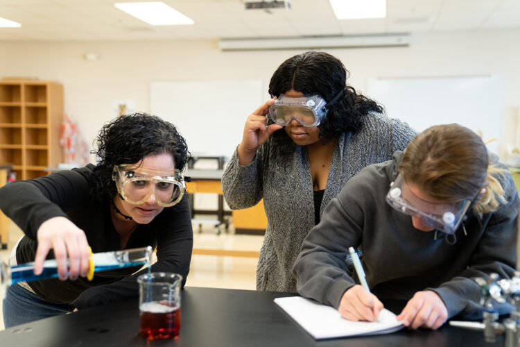 students in a science lab wearing goggles and using beakers