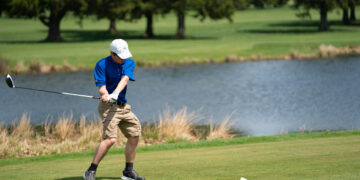 young man in blue polo hits golf ball with club on a golf course