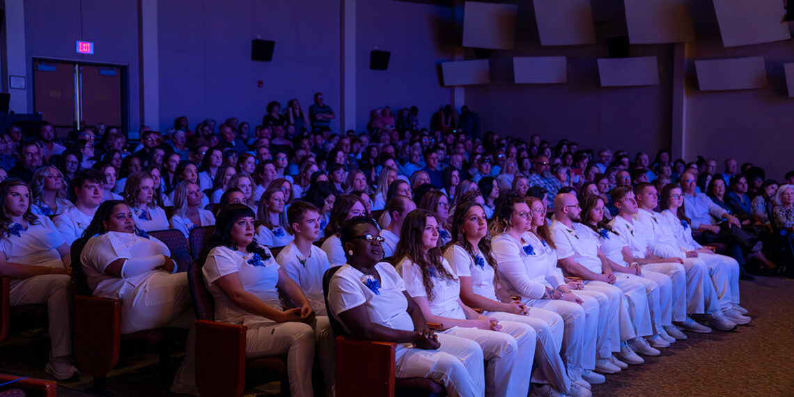 large group of people sitting in auditorium including graduates of bc3 nursing program in white uniforms