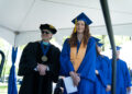 man in black cap and gown wearing sunglasses with woman in blue cap and gown at under a tent at a BC3 commencement ceremony